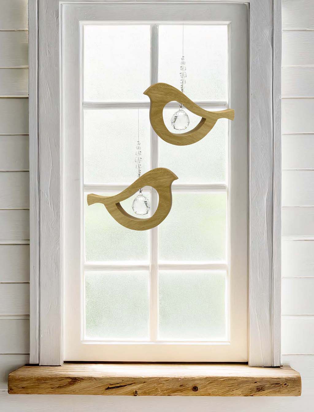 Two wooden bird shaped suncatchers hanging from wires with a large faceted crystals in the centre and smaller crystal beads on top. Hanging in front of a window