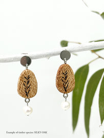 handmade wood and freshwater pearl earrings hanging from a stick  with eucalyptus in the background