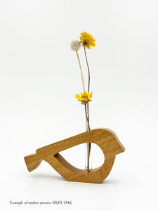 A wooden bird shaped vase with a glass test tube containing a yellow daisy and billy button sprig made from Silky Oak timber on white background