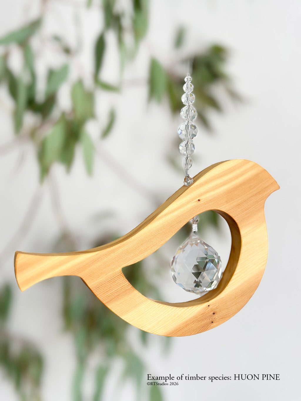 Wooden bird-shaped ornament with a crystal ball hanging against a blurred green foliage background.