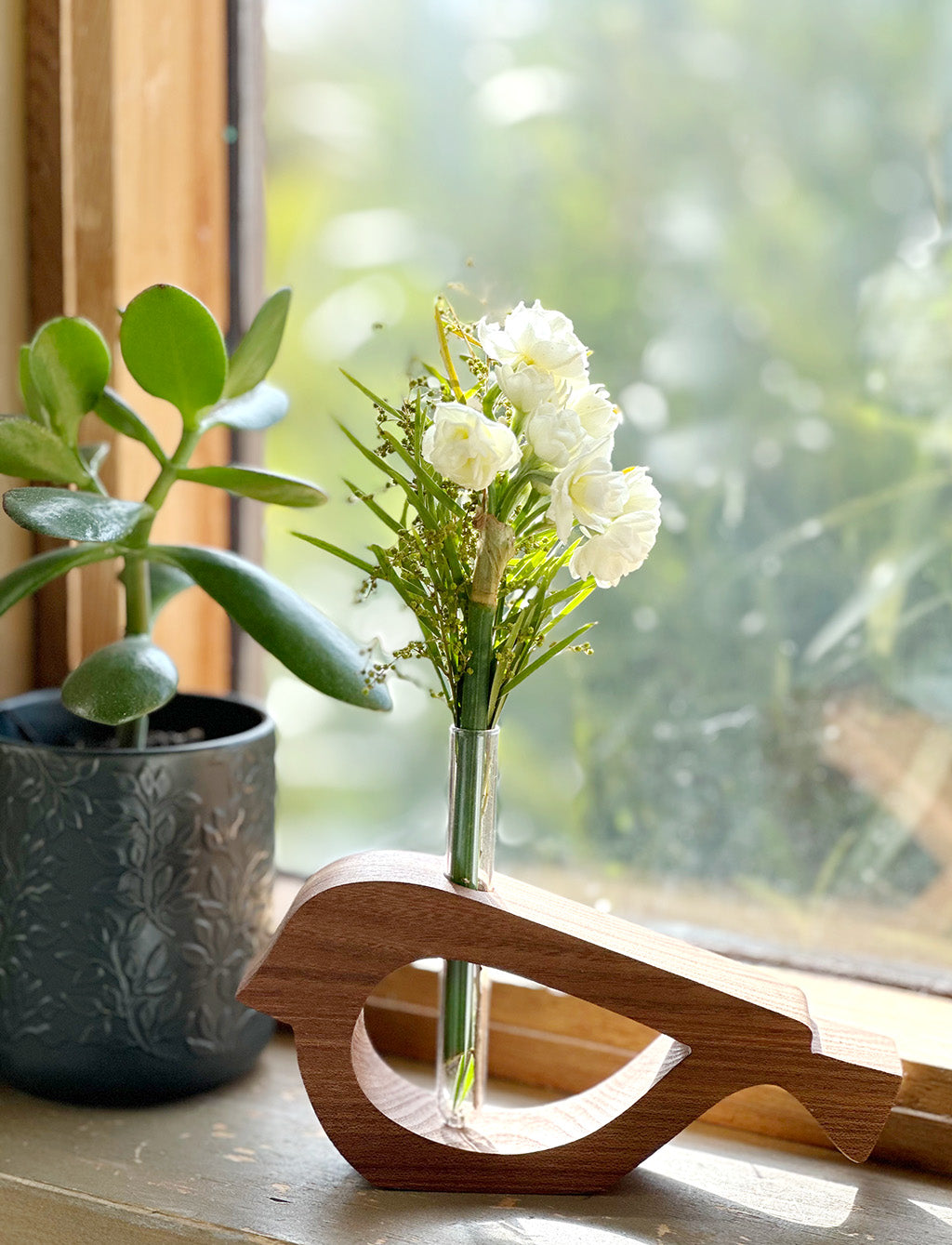 A wooden bird shaped vase with a sprig of jonquil and wattle made from Elm timber on a windowsill