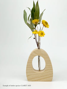 A wooden dome shaped vase with a glass test tube containing a paper daisy and eucalyptus sprig made from Claret Ash timber on white background