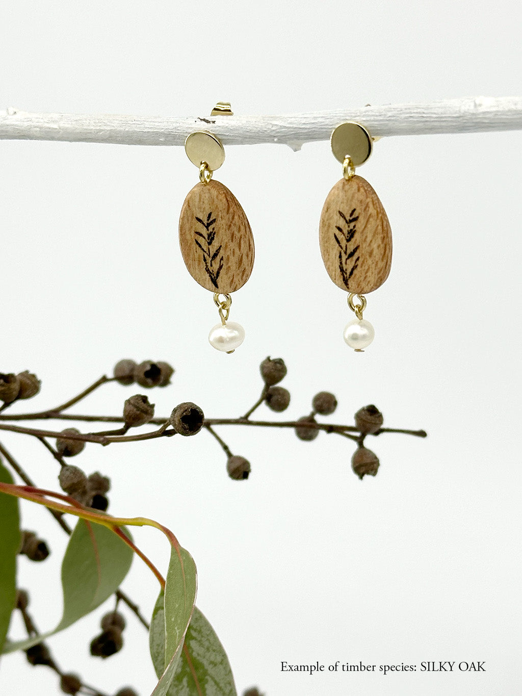 handmade wood and freshwater pearl earrings hanging from a stick  with eucalyptus in the background