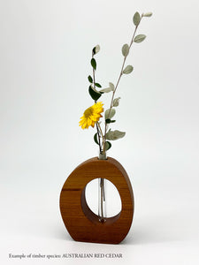 A wooden oval shaped vase with a glass test tube containing a Daisy sprig made from Australinan Red Cedar timber on white backgroun
