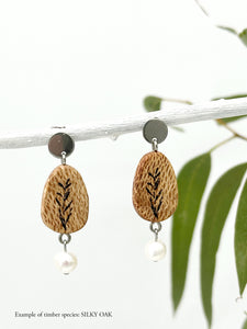 handmade wood and freshwater pearl earrings hanging from a stick  with eucalyptus in the background
