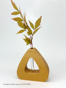 A wooden triangle shaped vase with a glass test tube containing a plant sprig made from Huon Pine timber on a white background