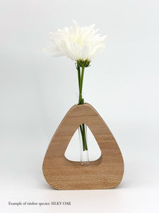 A wooden triangle shaped vase with a glass test tube containing a Daisy flower made from Silky Oak timber on a white background