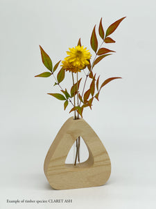 A wooden triangle shaped vase with a glass test tube containing a plant sprig made from Claret Ash timber on a white background