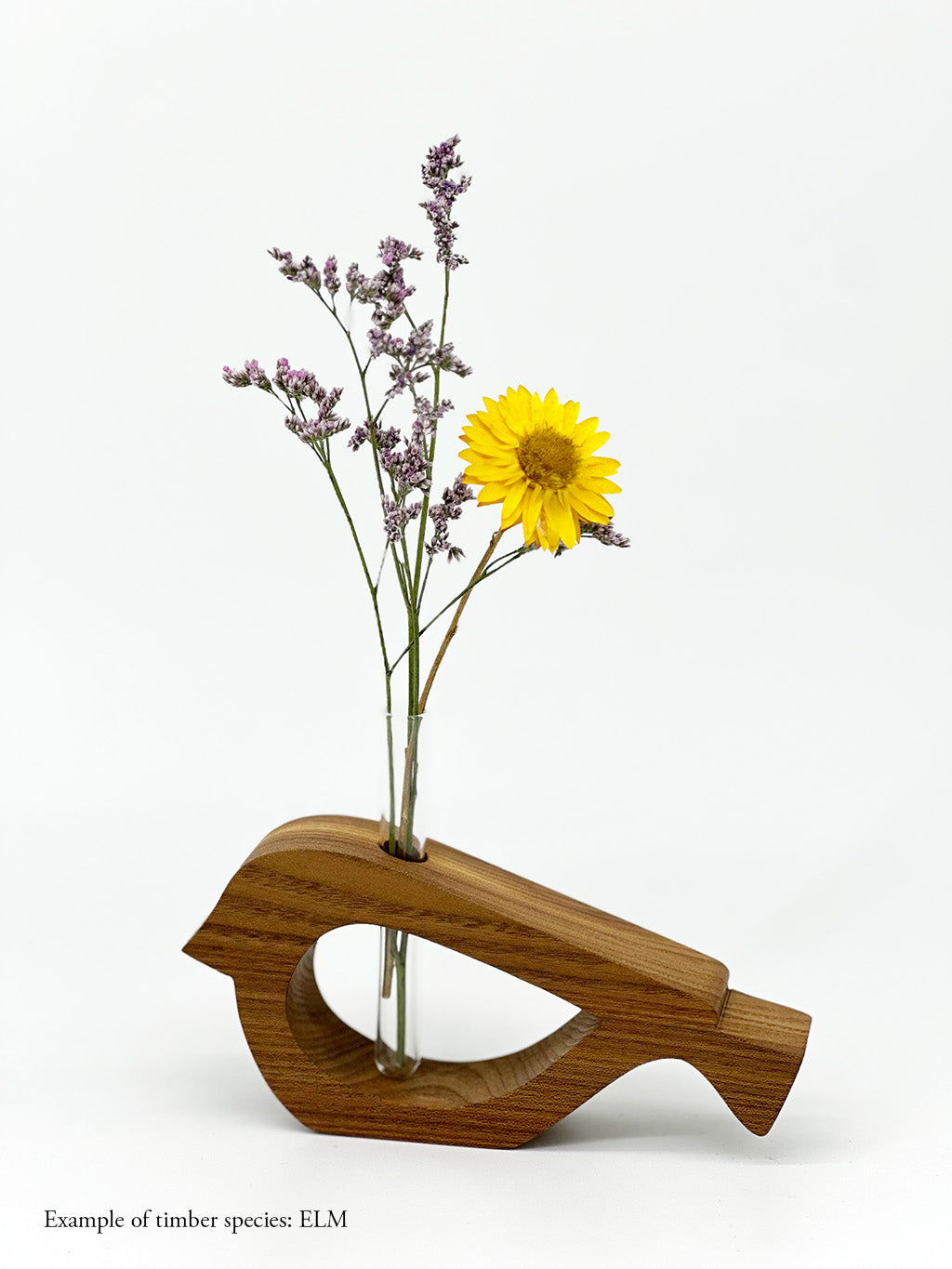 A wooden bird shaped vase with a glass test tube containing a yellow daisy and plant sprig made from Elm timber on white background