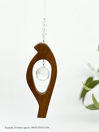 A wooden bird shaped suncatcher made from Spotted Gum hanging from a wire with a large faceted crystal in the centre and smaller crystal beads on top. 